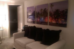 Acrylic print of palm trees in front of multicolored buildings seperated into three panels.