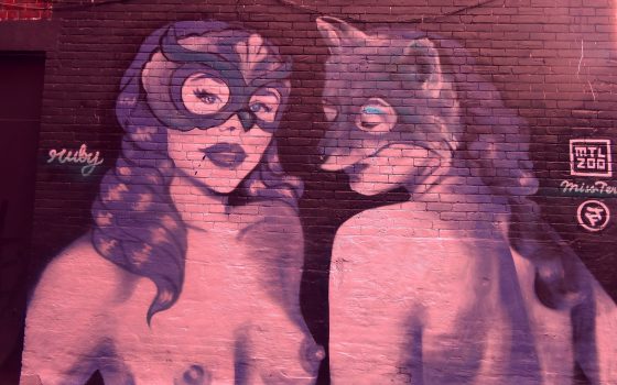 Graffiti art of two topless women wearing masks.
