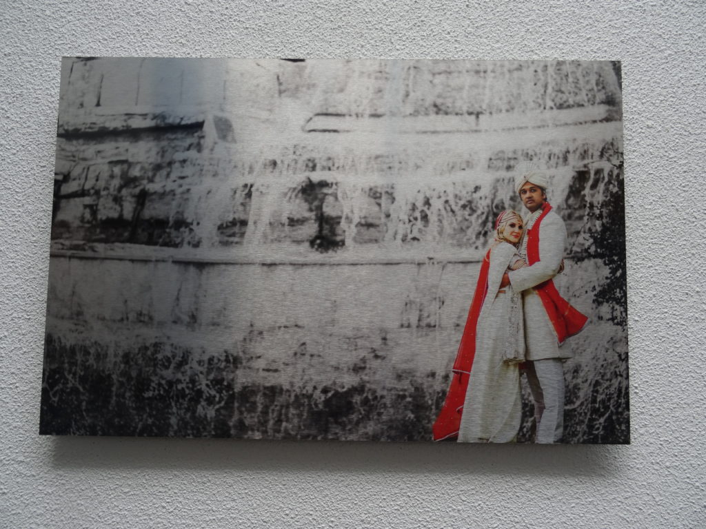 White metal print of wedding couple standing in front of massive rock formation.
